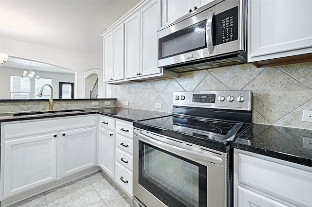 kitchen with dark stone countertops, sink, an inviting chandelier, white cabinetry, and appliances with stainless steel finishes