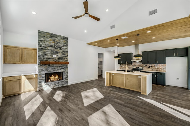 kitchen with wall chimney exhaust hood, a center island with sink, decorative light fixtures, stainless steel range oven, and high vaulted ceiling