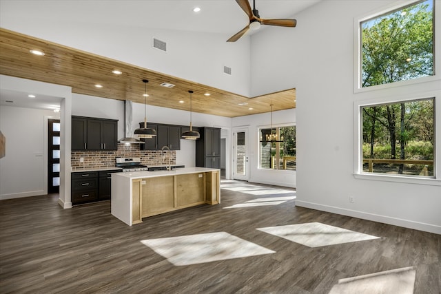 kitchen featuring dark hardwood / wood-style flooring, pendant lighting, stainless steel stove, high vaulted ceiling, and a kitchen island with sink