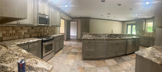 kitchen featuring stone counters, a center island, crown molding, backsplash, and appliances with stainless steel finishes