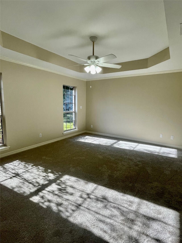 unfurnished room with a tray ceiling, dark colored carpet, ornamental molding, ceiling fan, and baseboards