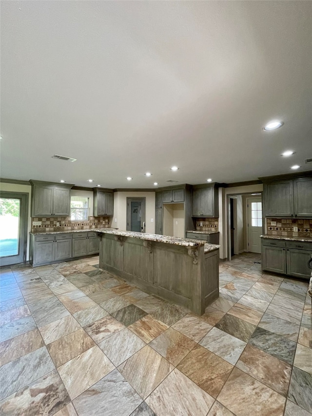 kitchen with light stone countertops, visible vents, backsplash, and a center island