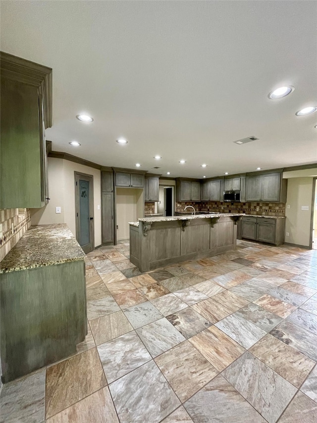 kitchen featuring crown molding, tasteful backsplash, stainless steel microwave, visible vents, and light stone countertops