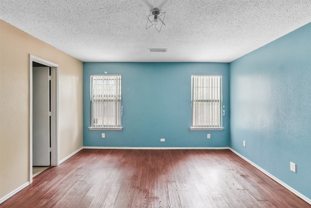 empty room with a healthy amount of sunlight, a textured ceiling, and hardwood / wood-style floors