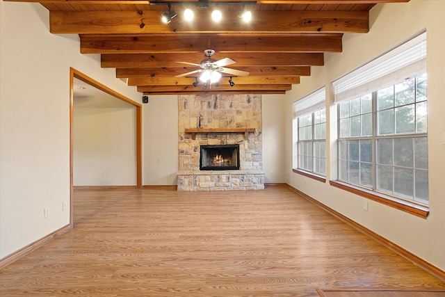 unfurnished living room featuring a stone fireplace, beam ceiling, a healthy amount of sunlight, and light wood-type flooring