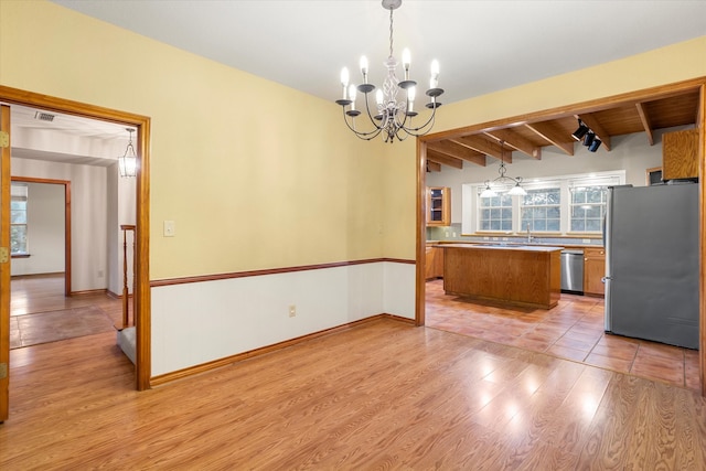 kitchen with a kitchen island, hanging light fixtures, a chandelier, appliances with stainless steel finishes, and light hardwood / wood-style floors