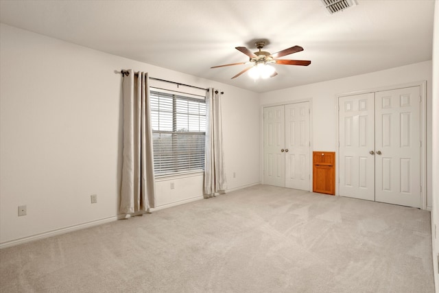 unfurnished bedroom featuring multiple closets, light colored carpet, and ceiling fan