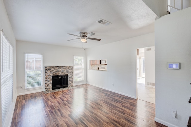 unfurnished living room featuring ceiling fan, a stone fireplace, wood-type flooring, and a wealth of natural light