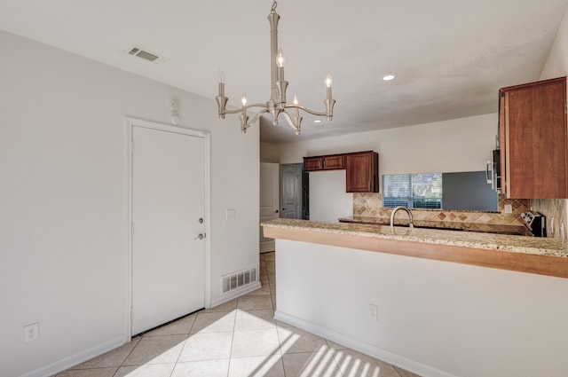 kitchen featuring decorative backsplash, light tile patterned floors, kitchen peninsula, range, and a chandelier