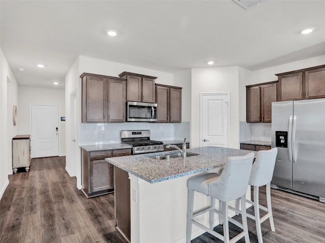 kitchen featuring sink, dark hardwood / wood-style flooring, an island with sink, stainless steel appliances, and light stone countertops