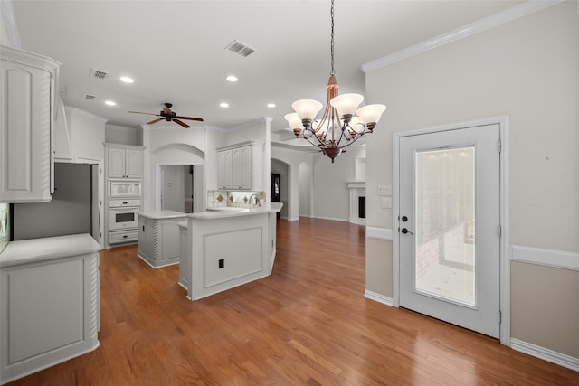 kitchen with a center island, white appliances, white cabinets, hanging light fixtures, and light hardwood / wood-style flooring