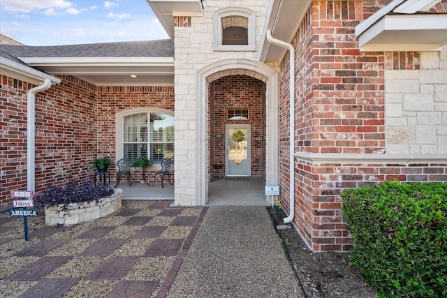 entrance to property with roof with shingles and brick siding