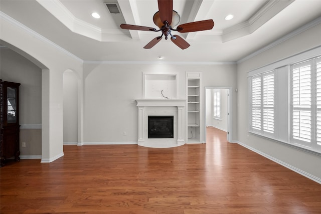 unfurnished living room featuring built in shelves, wood-type flooring, ornamental molding, and a raised ceiling