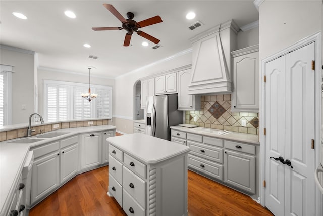 kitchen with stainless steel refrigerator with ice dispenser, premium range hood, ceiling fan with notable chandelier, sink, and hardwood / wood-style floors