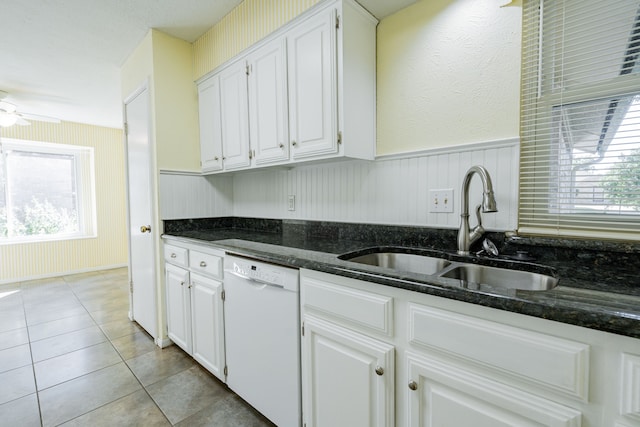 kitchen with white dishwasher, light tile patterned flooring, a sink, white cabinetry, and wainscoting