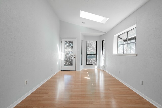 empty room with vaulted ceiling with skylight and light wood-type flooring