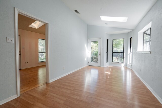 unfurnished room featuring a textured ceiling, light wood-type flooring, a healthy amount of sunlight, and vaulted ceiling with skylight