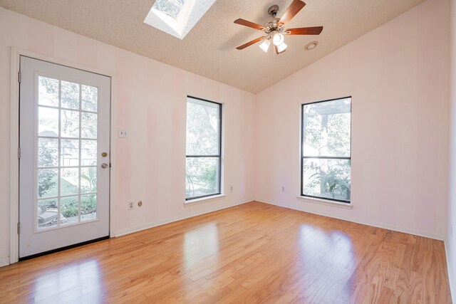 spare room featuring light hardwood / wood-style floors, a textured ceiling, and vaulted ceiling with skylight