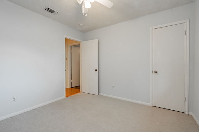 spare room with light carpet, a textured ceiling, visible vents, and baseboards