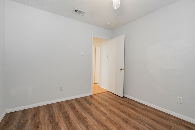 spare room featuring baseboards, a textured ceiling, visible vents, and wood finished floors