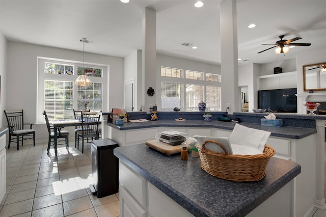 kitchen featuring ceiling fan with notable chandelier, a kitchen island, pendant lighting, white cabinets, and light tile patterned floors