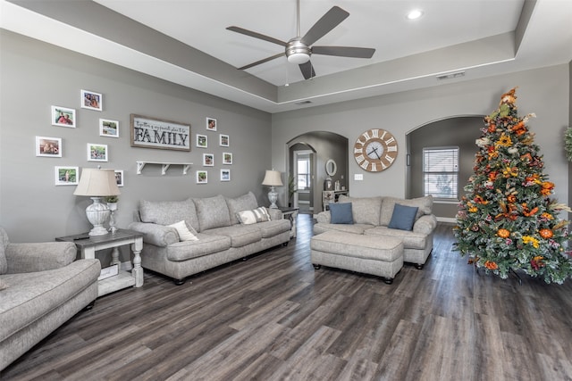 living room featuring dark wood-type flooring, ceiling fan, a healthy amount of sunlight, and a raised ceiling