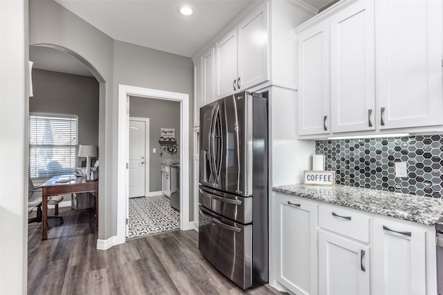 kitchen featuring light stone countertops, backsplash, stainless steel fridge, white cabinetry, and dark wood-type flooring