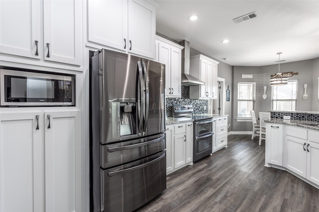 kitchen featuring wall chimney range hood, light stone countertops, appliances with stainless steel finishes, white cabinetry, and dark wood-type flooring