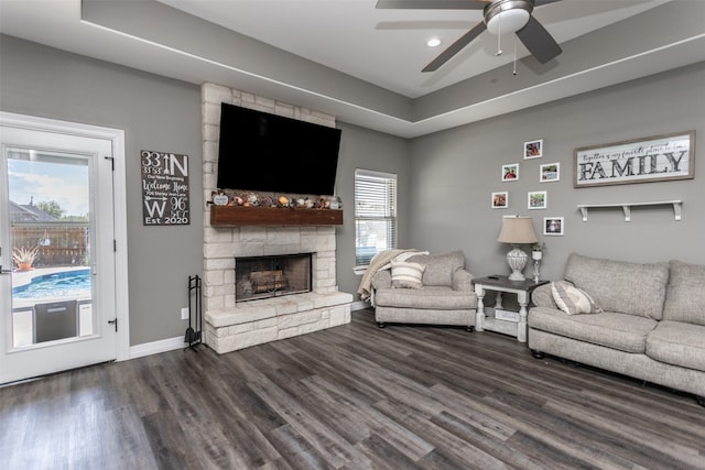 living room with dark wood-type flooring, ceiling fan, a stone fireplace, and a wealth of natural light