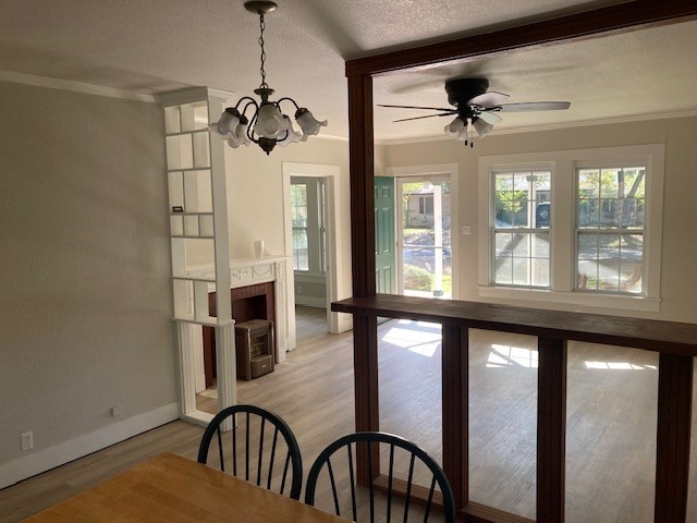 dining room with light hardwood / wood-style flooring, a textured ceiling, a fireplace, ceiling fan with notable chandelier, and ornamental molding