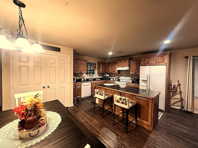 kitchen with pendant lighting, a center island, white appliances, dark hardwood / wood-style floors, and a breakfast bar area