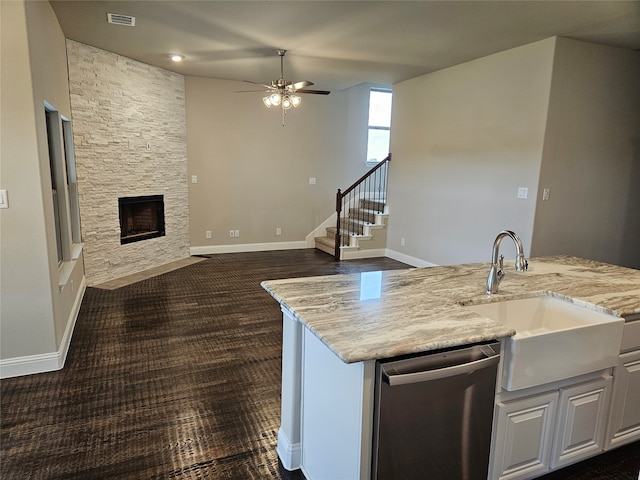 kitchen with a fireplace, white cabinetry, sink, stainless steel dishwasher, and light stone countertops