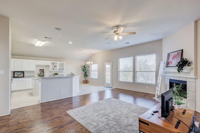 living room featuring vaulted ceiling, a fireplace, ceiling fan with notable chandelier, and light wood-type flooring