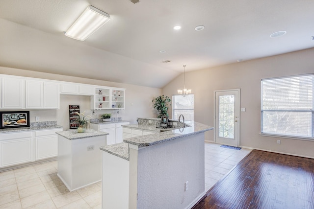 kitchen with white cabinetry, vaulted ceiling, hanging light fixtures, a center island with sink, and light stone countertops