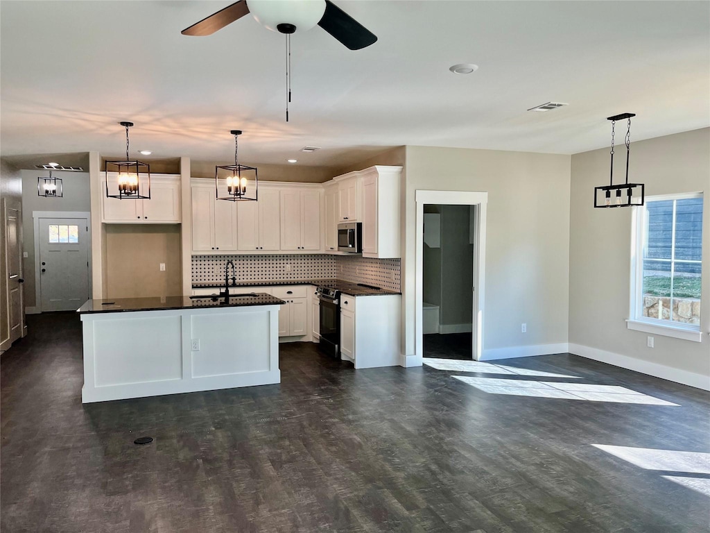 kitchen with pendant lighting, black / electric stove, white cabinets, and a center island with sink