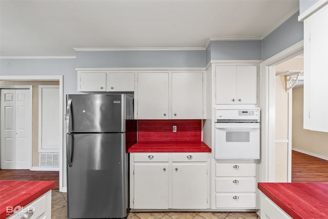 kitchen with white cabinets, stainless steel fridge, oven, and crown molding