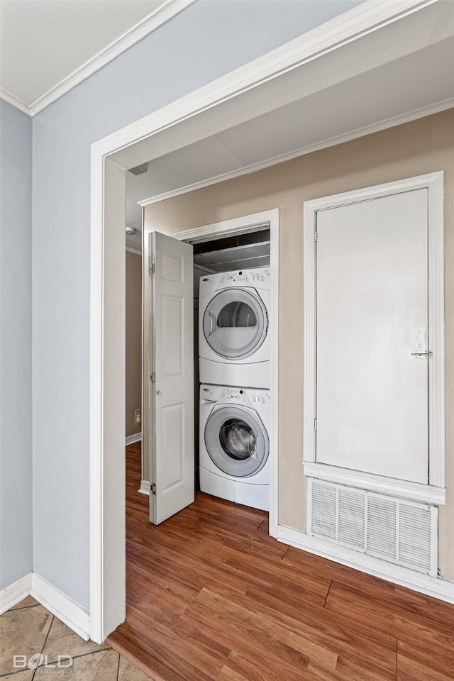 clothes washing area with crown molding, wood-type flooring, and stacked washer and dryer