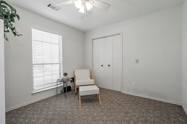 sitting room featuring a wealth of natural light, ceiling fan, and dark colored carpet