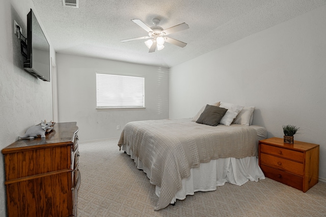 bedroom with ceiling fan, light carpet, and a textured ceiling