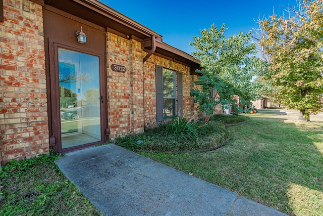 property entrance featuring a yard and brick siding