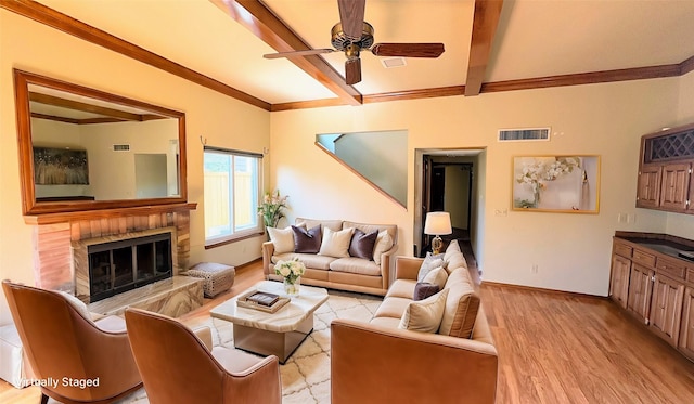 living room with a fireplace, beam ceiling, ceiling fan, and light wood-type flooring