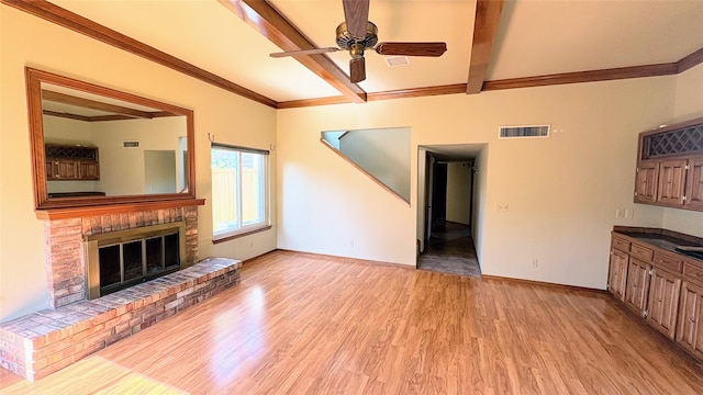 unfurnished living room featuring ceiling fan, a brick fireplace, beam ceiling, light wood-type flooring, and ornamental molding