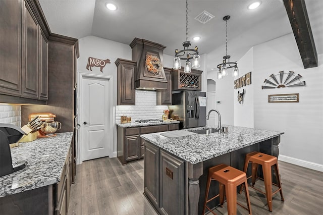 kitchen with lofted ceiling, backsplash, a center island with sink, sink, and appliances with stainless steel finishes