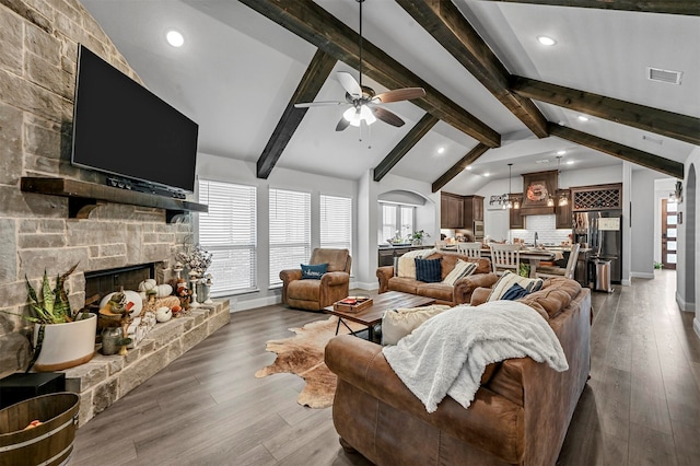 living room with a stone fireplace, hardwood / wood-style floors, lofted ceiling with beams, and ceiling fan with notable chandelier