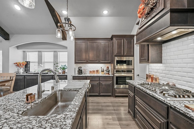 kitchen with tasteful backsplash, sink, light wood-type flooring, stainless steel appliances, and custom range hood