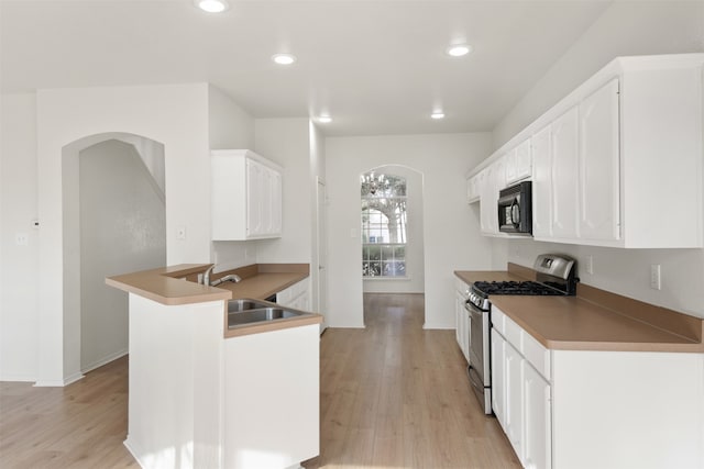 kitchen featuring kitchen peninsula, sink, light hardwood / wood-style flooring, white cabinets, and stainless steel range with gas cooktop