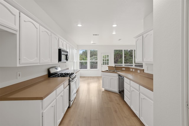 kitchen featuring white gas range, white cabinetry, sink, and light hardwood / wood-style floors