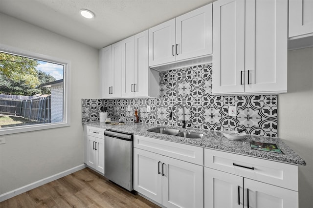 kitchen with tasteful backsplash, sink, stainless steel dishwasher, white cabinets, and light hardwood / wood-style flooring