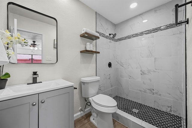 bathroom with a tile shower, toilet, ceiling fan, vanity, and hardwood / wood-style flooring