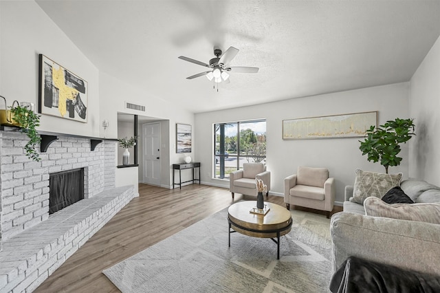 living room with ceiling fan, a textured ceiling, hardwood / wood-style flooring, vaulted ceiling, and a fireplace